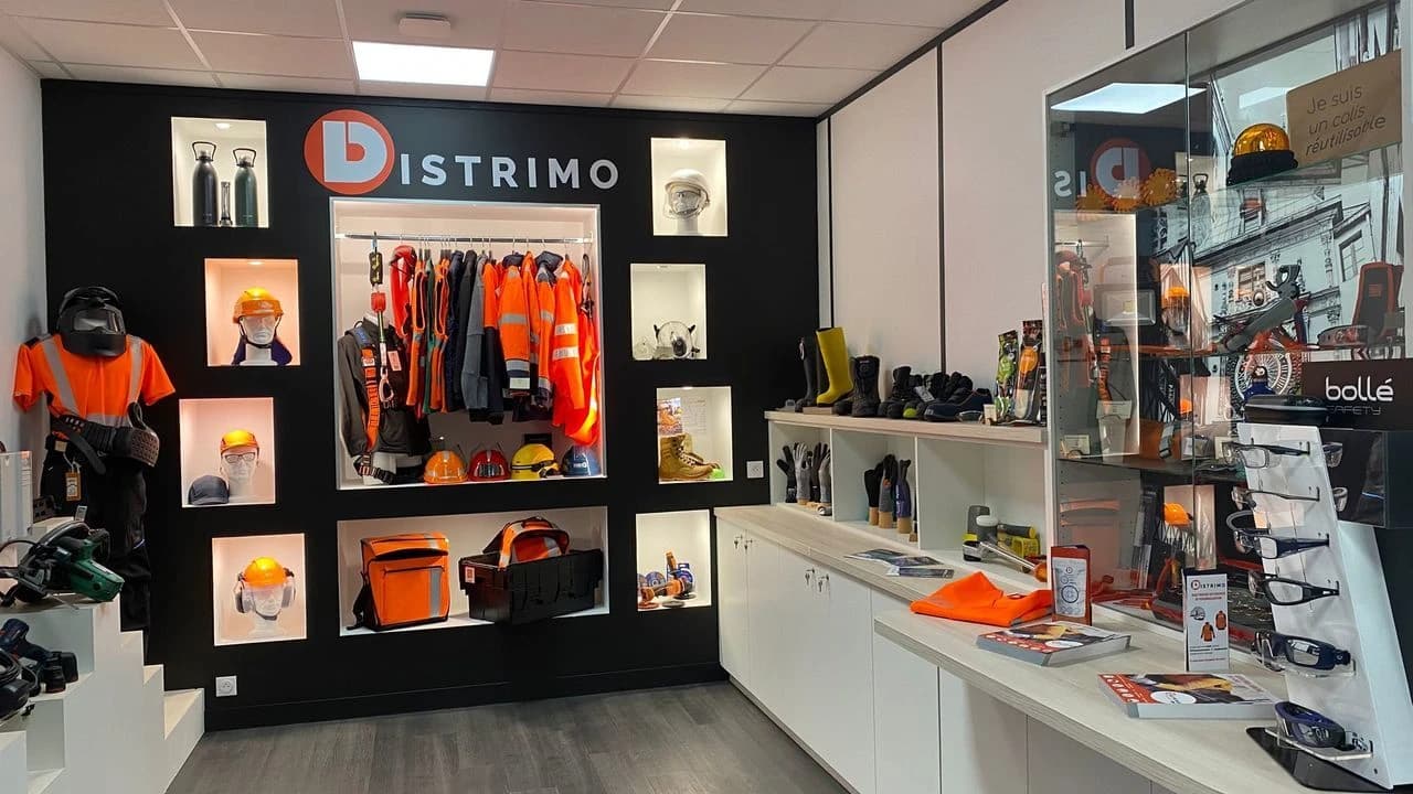 Intérieur d'un magasin Distrimo présentant des vêtements de travail et équipements de protection individuelle (EPI), avec des mannequins portant des gilets de sécurité, des casques, des harnais, et des étagères remplies de bottes, gants, lunettes et autres accessoires.