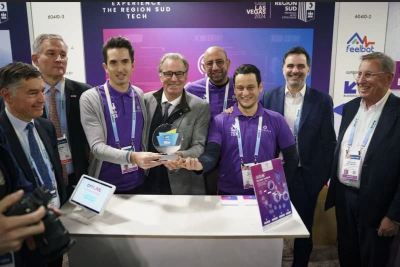A group of eight men, several wearing purple polo shirts, smiles as three of them jointly hold a clear glass trophy with blue and yellow accents. They are at an exhibition booth with "Region Sud Tech" and "Las Vegas 2024" banners in the background.