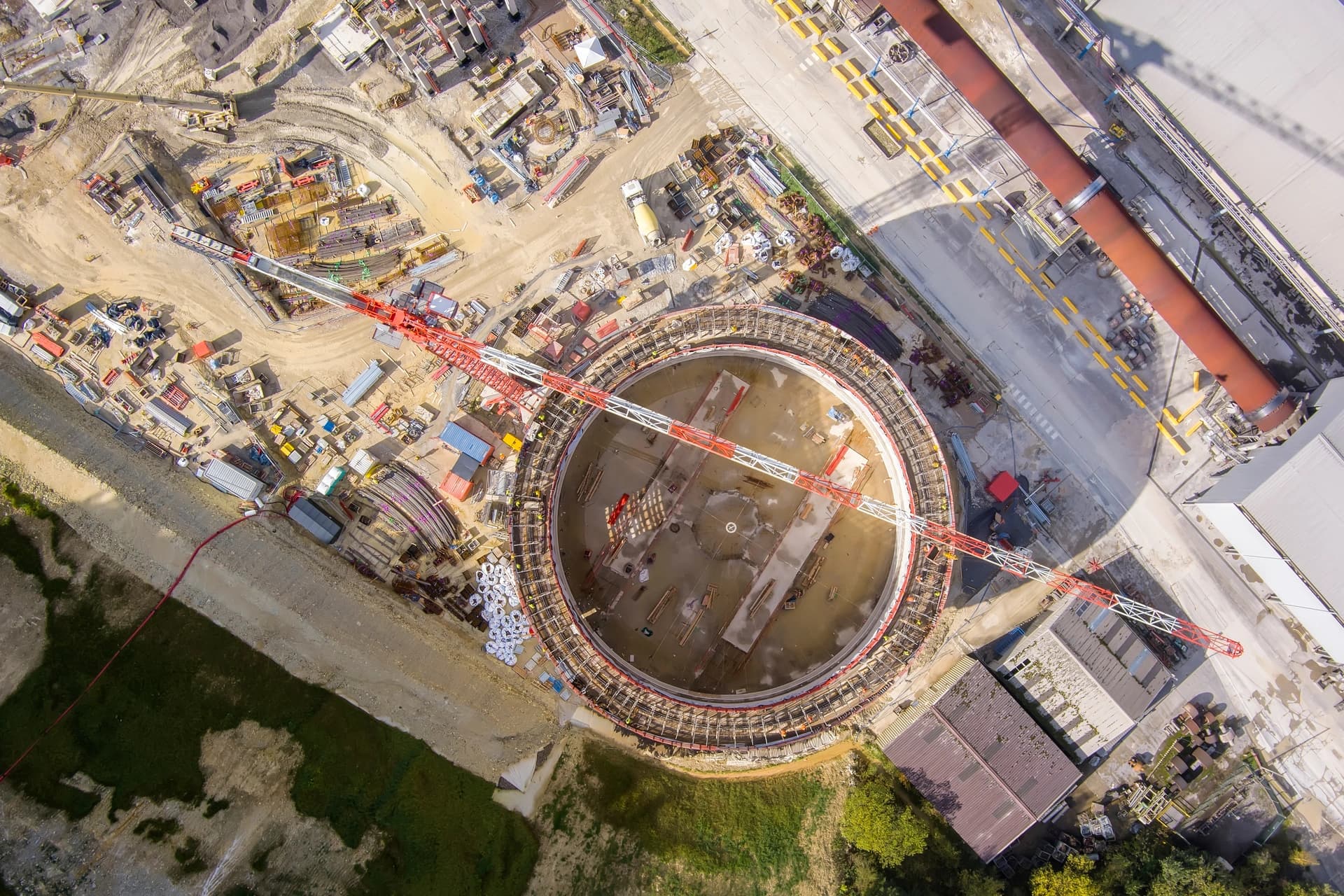 Vue aérienne d'un chantier industriel circulaire avec une grue rouge et blanche en surplomb.
