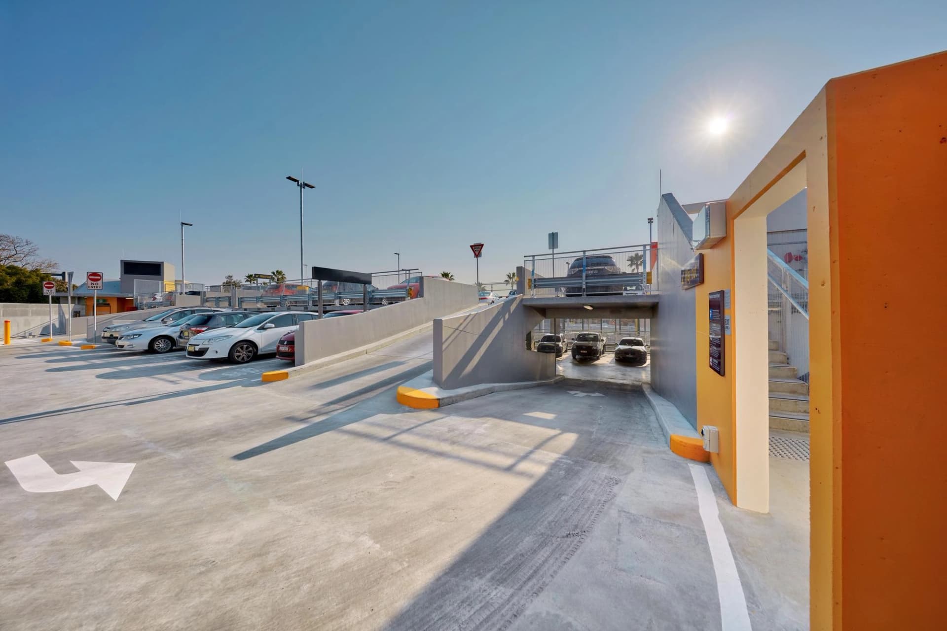 Parking à étages en plein air avec rampes d'accès et voitures garées par une journée ensoleillée.