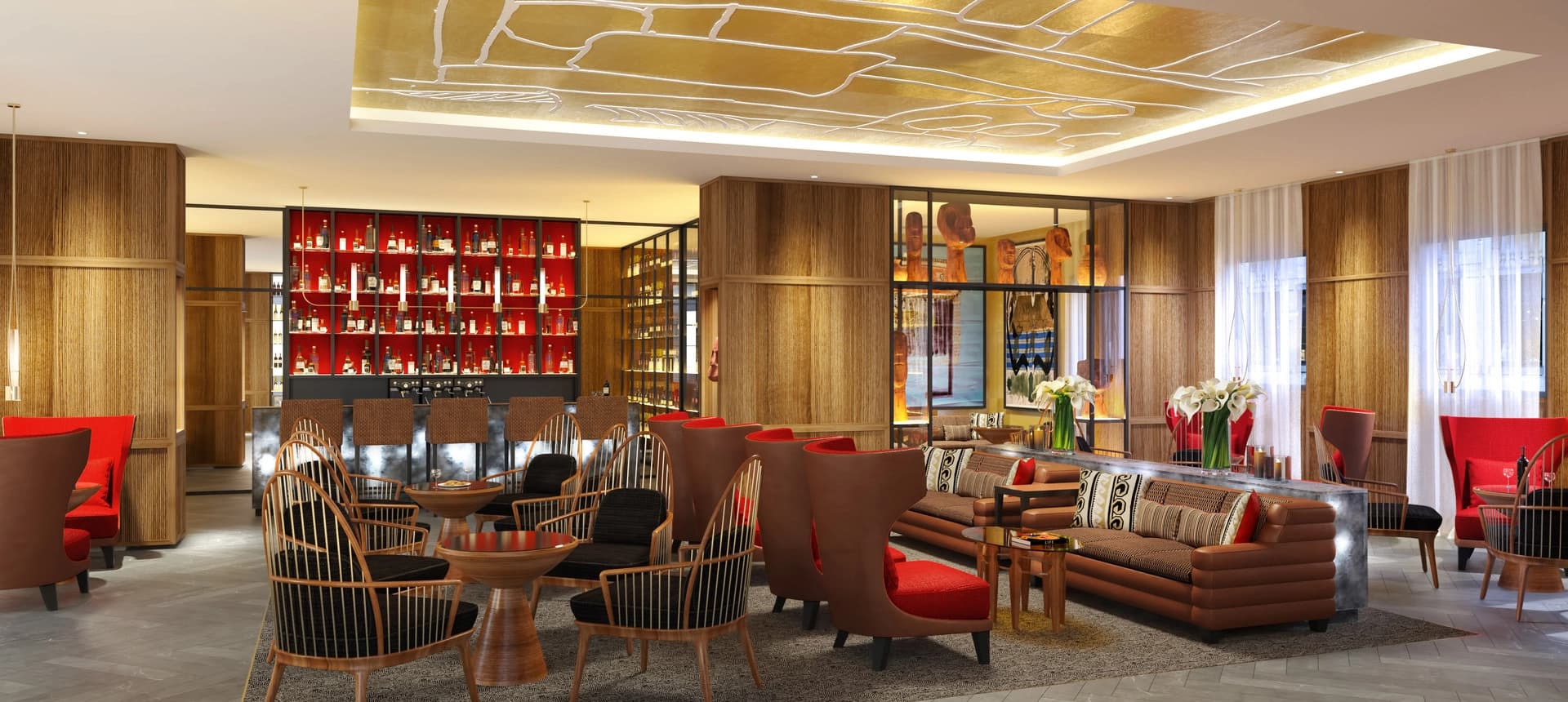 Un salon d'hôtel luxueux et moderne présente un bar éclairé en rouge vif rempli de bouteilles, entouré de canapés en cuir marron, de fauteuils rouges et de chaises en bois. L'espace est agrémenté de murs en bois lambrissé, d'un plafond doré à motifs abstraits et de sculptures en bois dans des vitrines, créant une ambiance sophistiquée et chaleureuse.