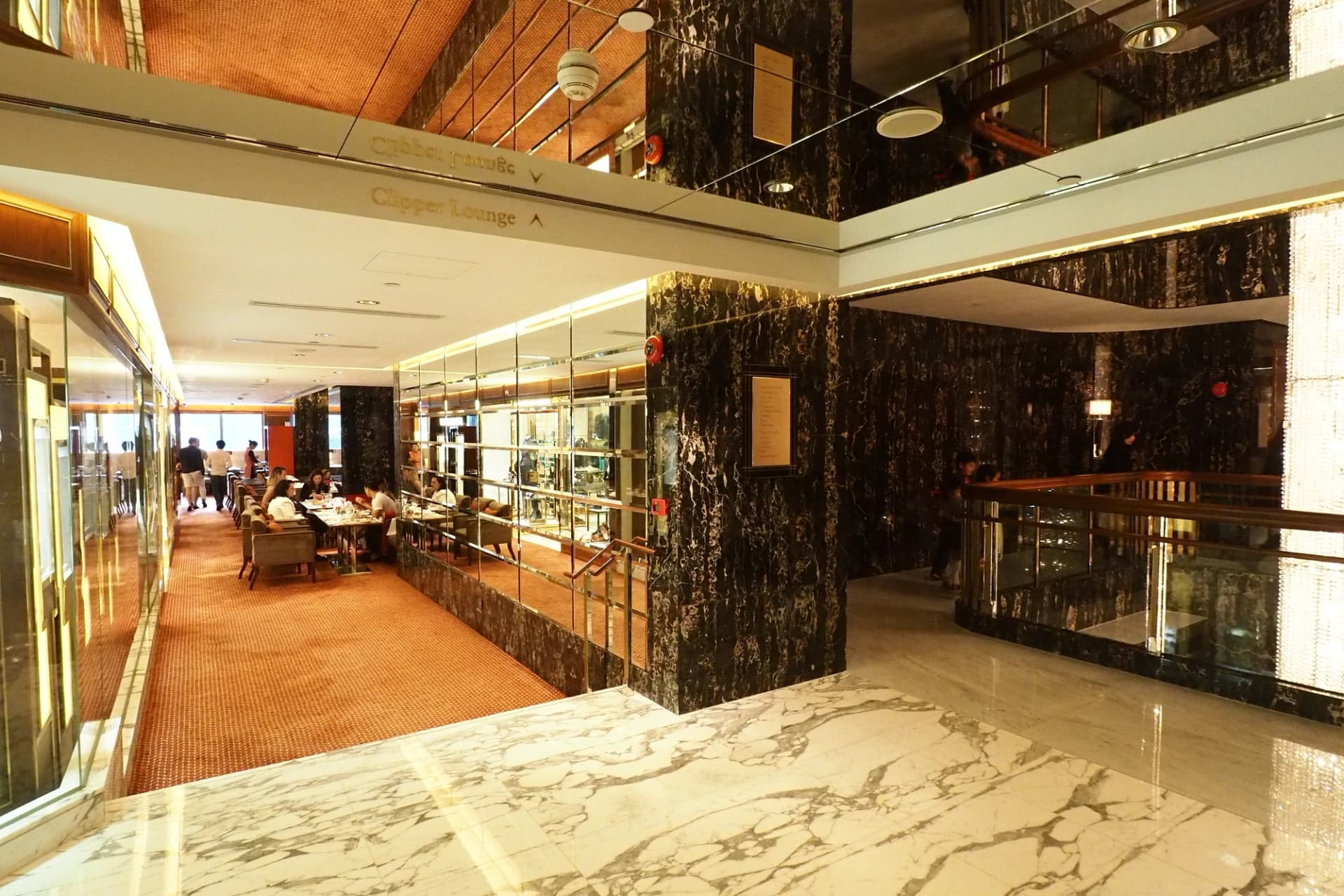 Salon d'hôtel luxueux avec sols en marbre, murs en miroir et clients d'un espace de restauration élégant.