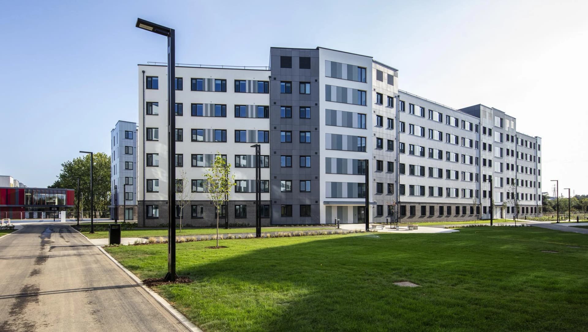 Immeuble moderne à plusieurs étages avec façades blanches et grises, une pelouse verte et des lampadaires noirs épurés.