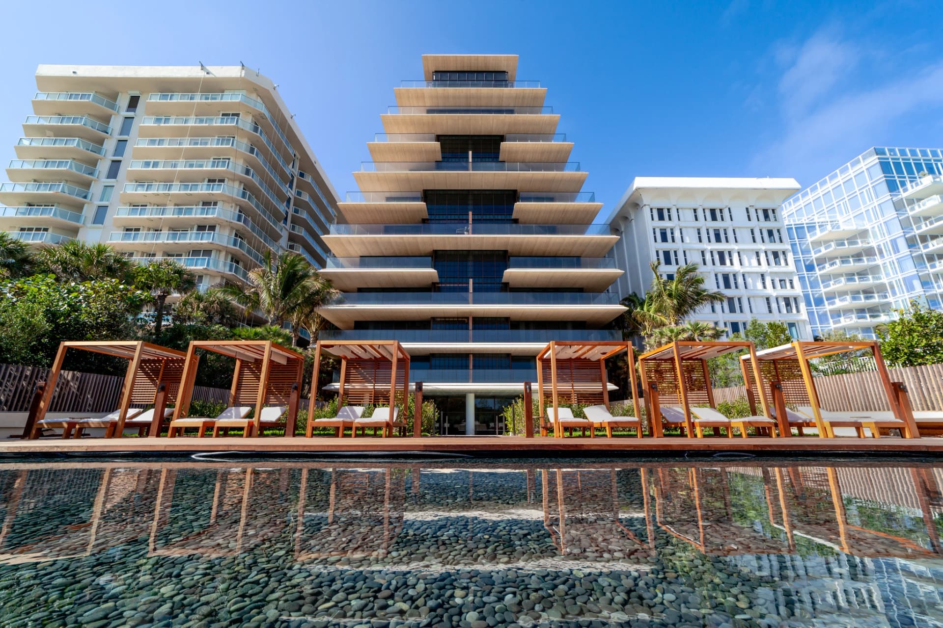 Immeuble moderne en forme de pyramide avec cabanas en bois et piscine de galets sous un ciel bleu.
