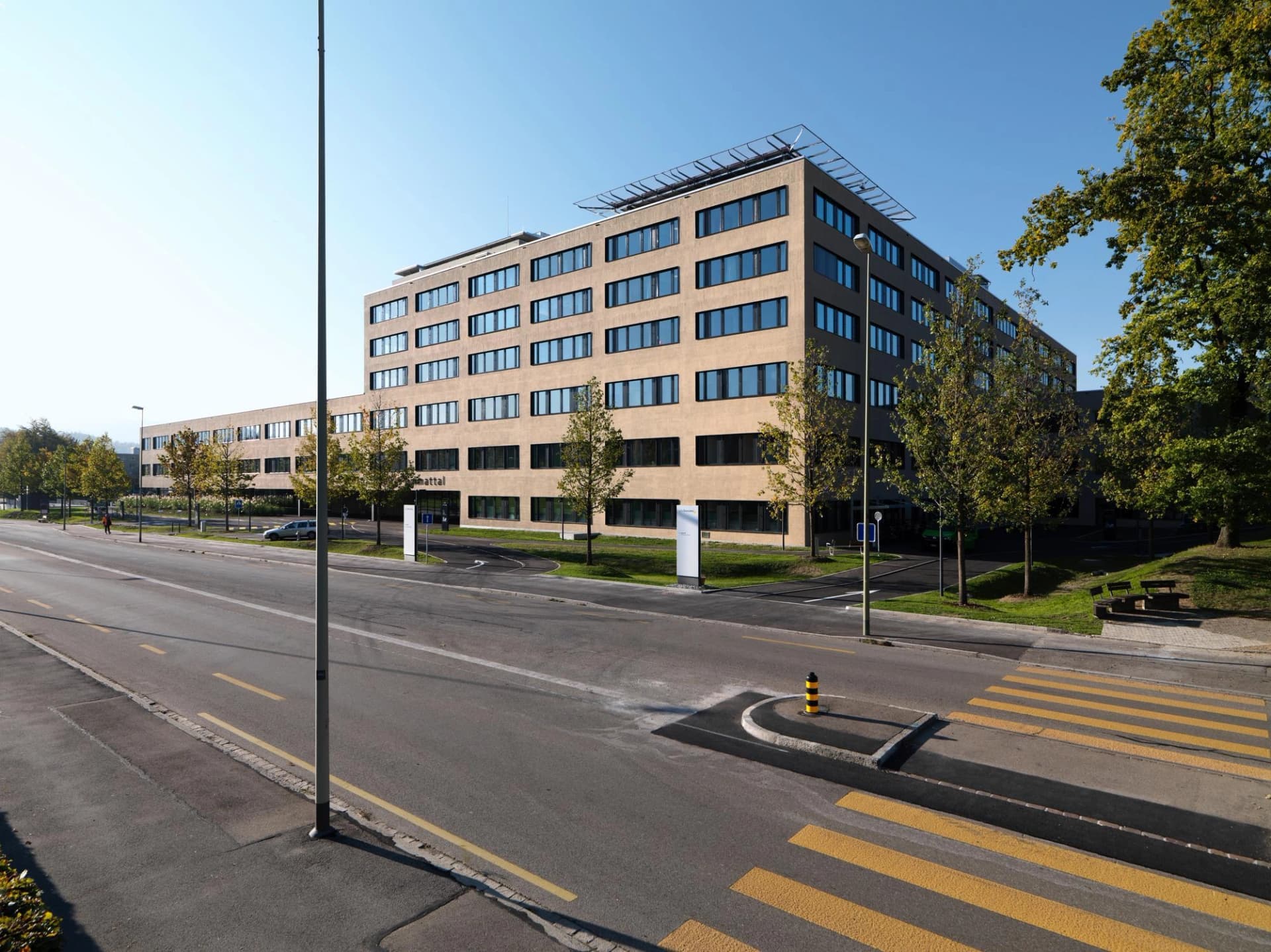 Un grand bâtiment moderne avec un héliport sur le toit, situé à côté d'une route et d'un passage piéton.