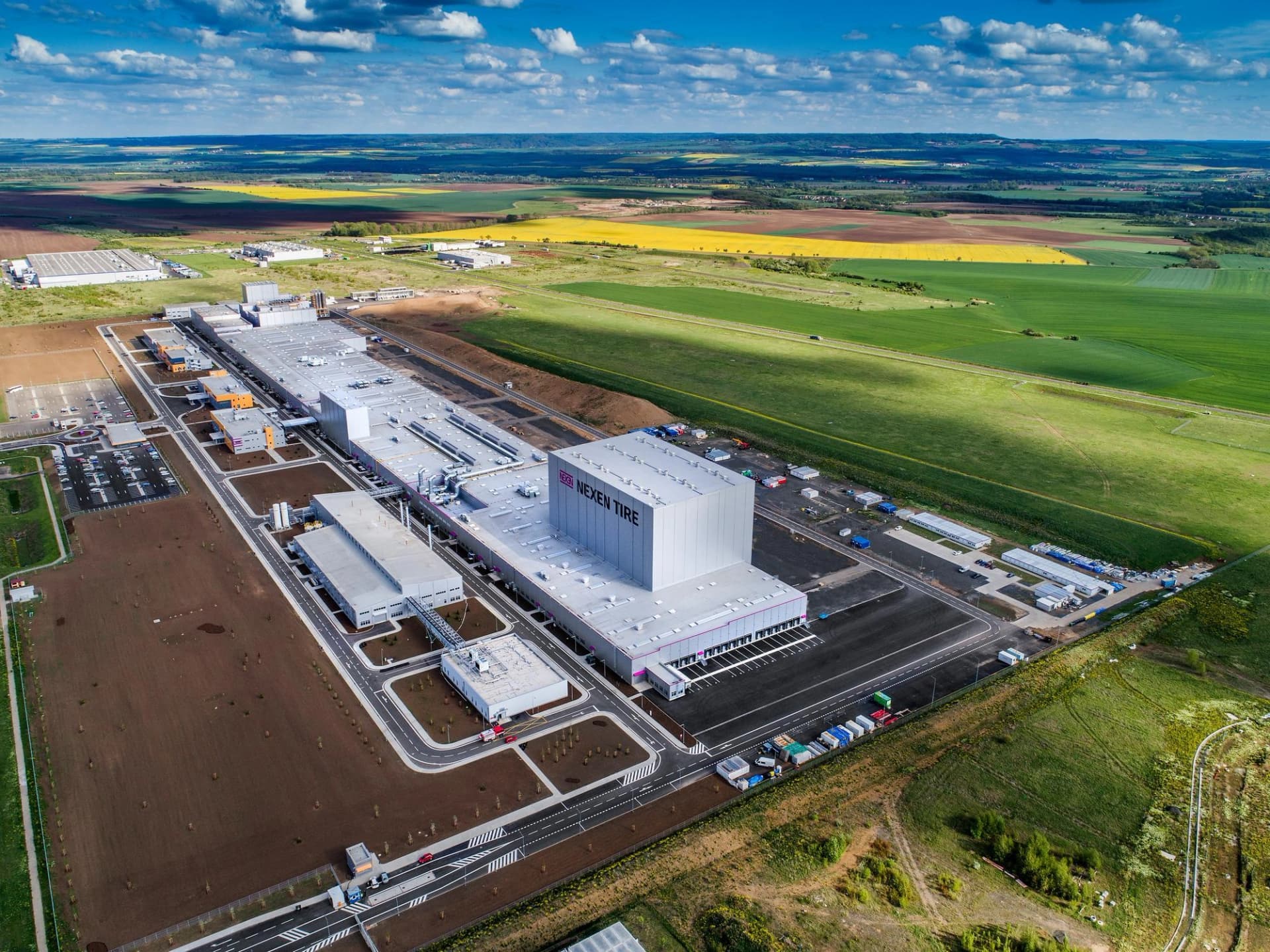 Vue aérienne d'un grand complexe industriel Nexen Tire situé dans un paysage rural aux champs colorés.